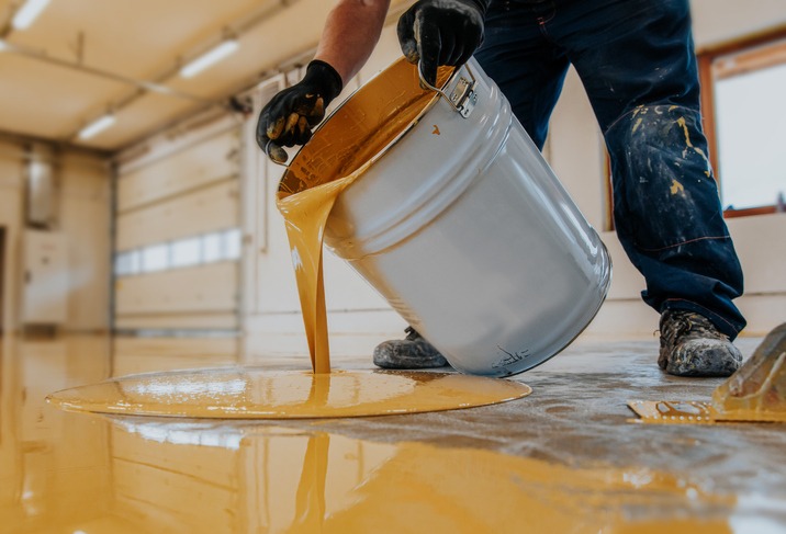 Worker applying a yellow epoxy resin bucket on floor for the final coat.