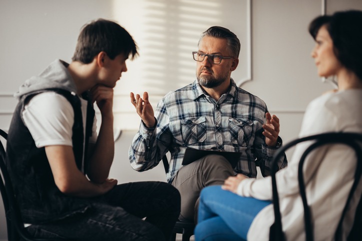 Psychologist talking to depressed teenager and his mum during therapy session