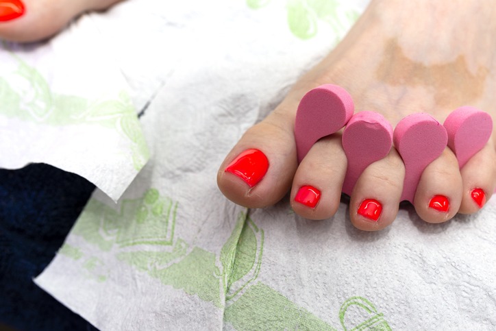 Hybrid nails painted red at the feet, separated by a pink spacer.