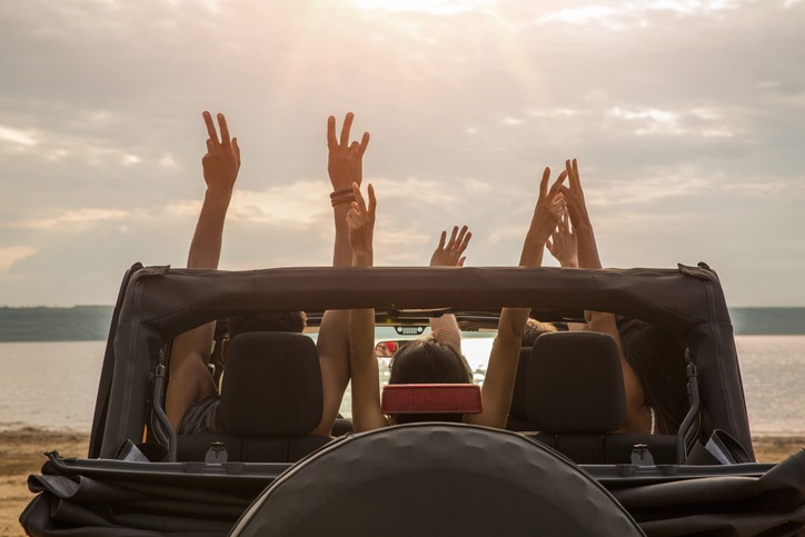 Friends sitting in a car with hands raised