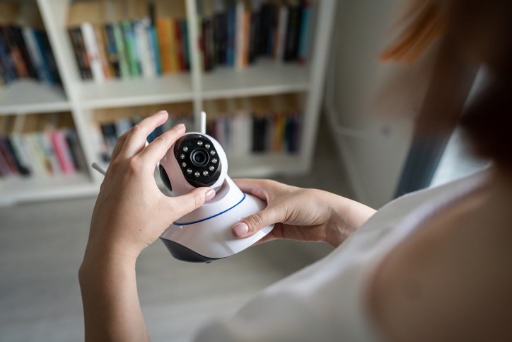 Close up on midsection and hands of unknown caucasian woman holding home security surveillance camera while standing in room adjusting and setting up equipment copy space