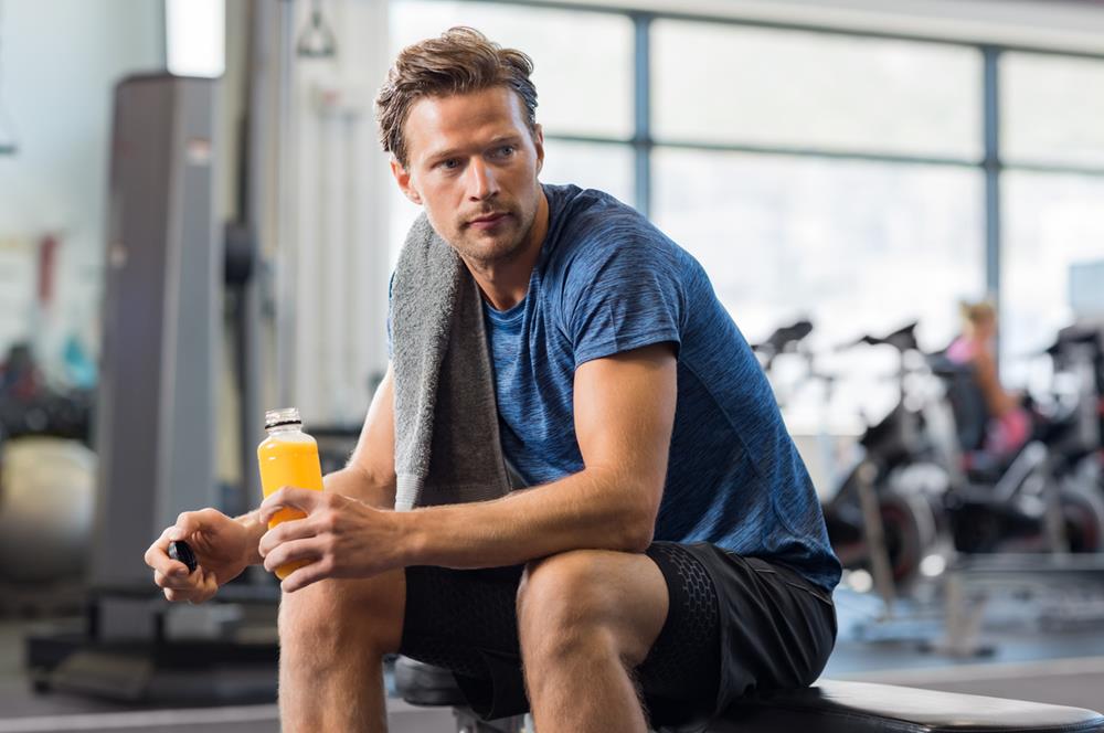Man in the gym drinking a bottle of orange juice