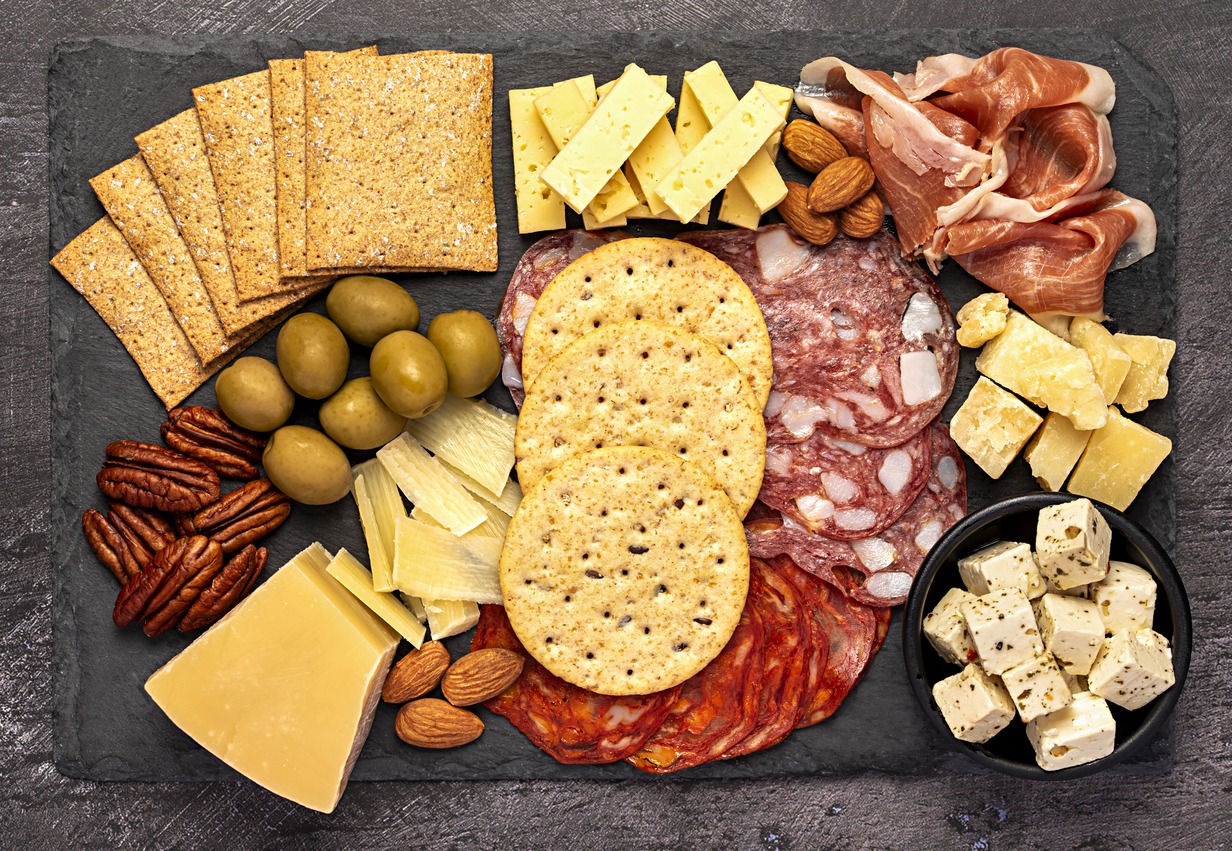 a platter of crackers, cheese, nuts, olives, and cold cuts