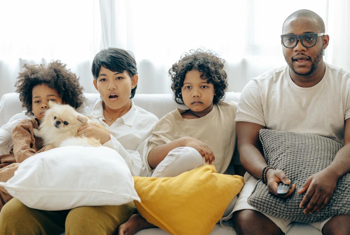 Interested multiracial family watching TV on the sofa together with a dog