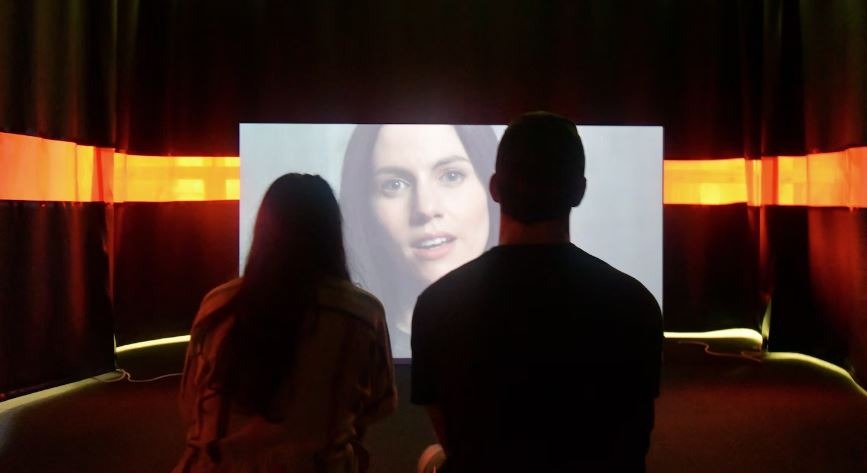 Two people mesmerized by a woman on TV screen