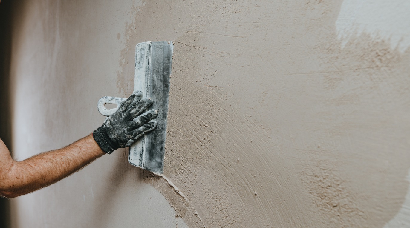 male builder in work overalls plastering a wall using a construction trowel with stucco