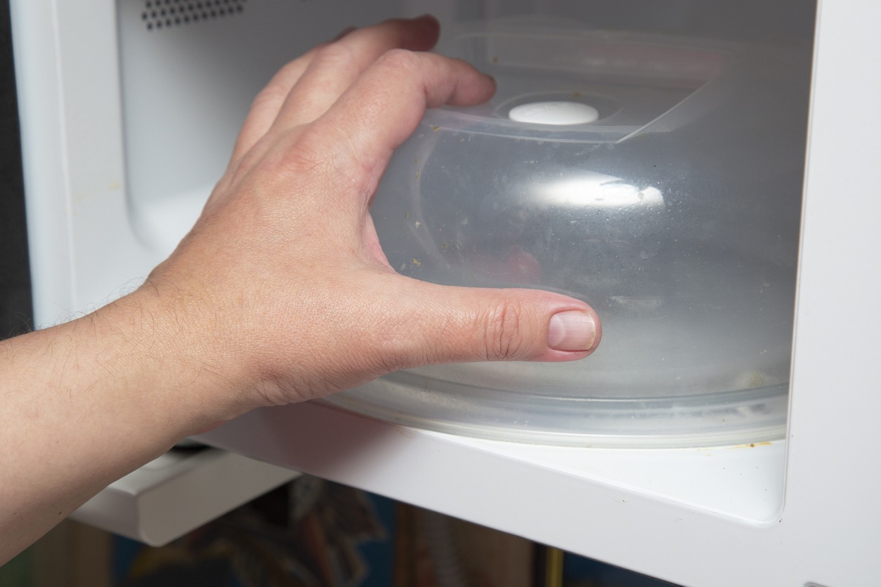 A person uses a microwave oven with a plastic food cover