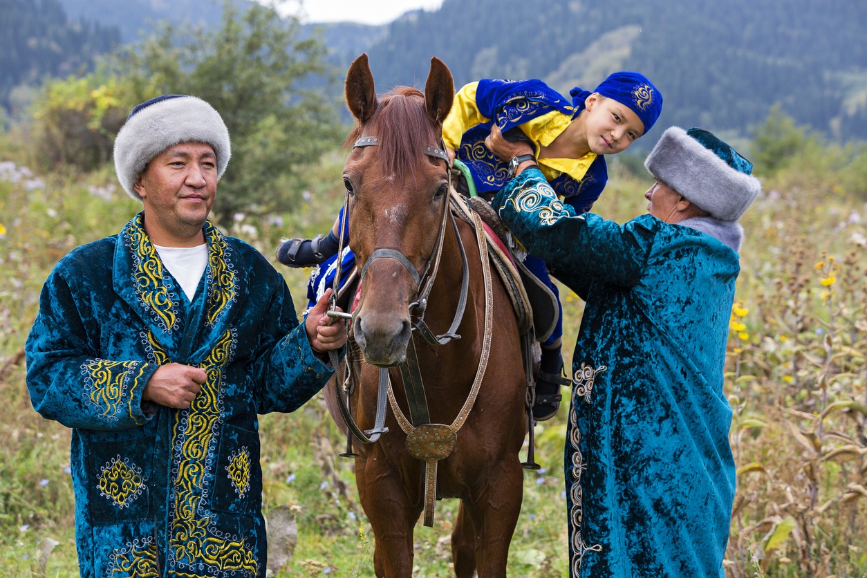 Kazakh men in national costumes helps the boy to get off his horse