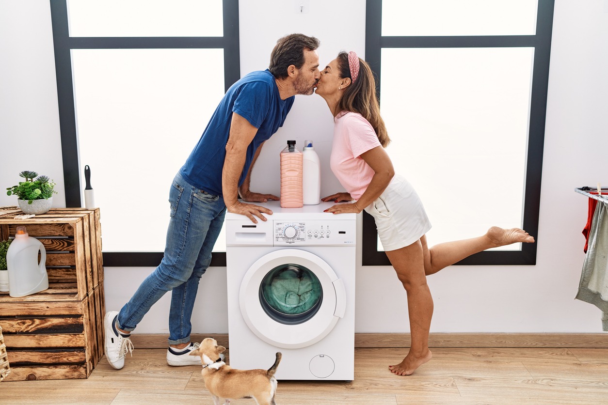 Middle age man and woman couple kissing and washing clothes at laundry room
