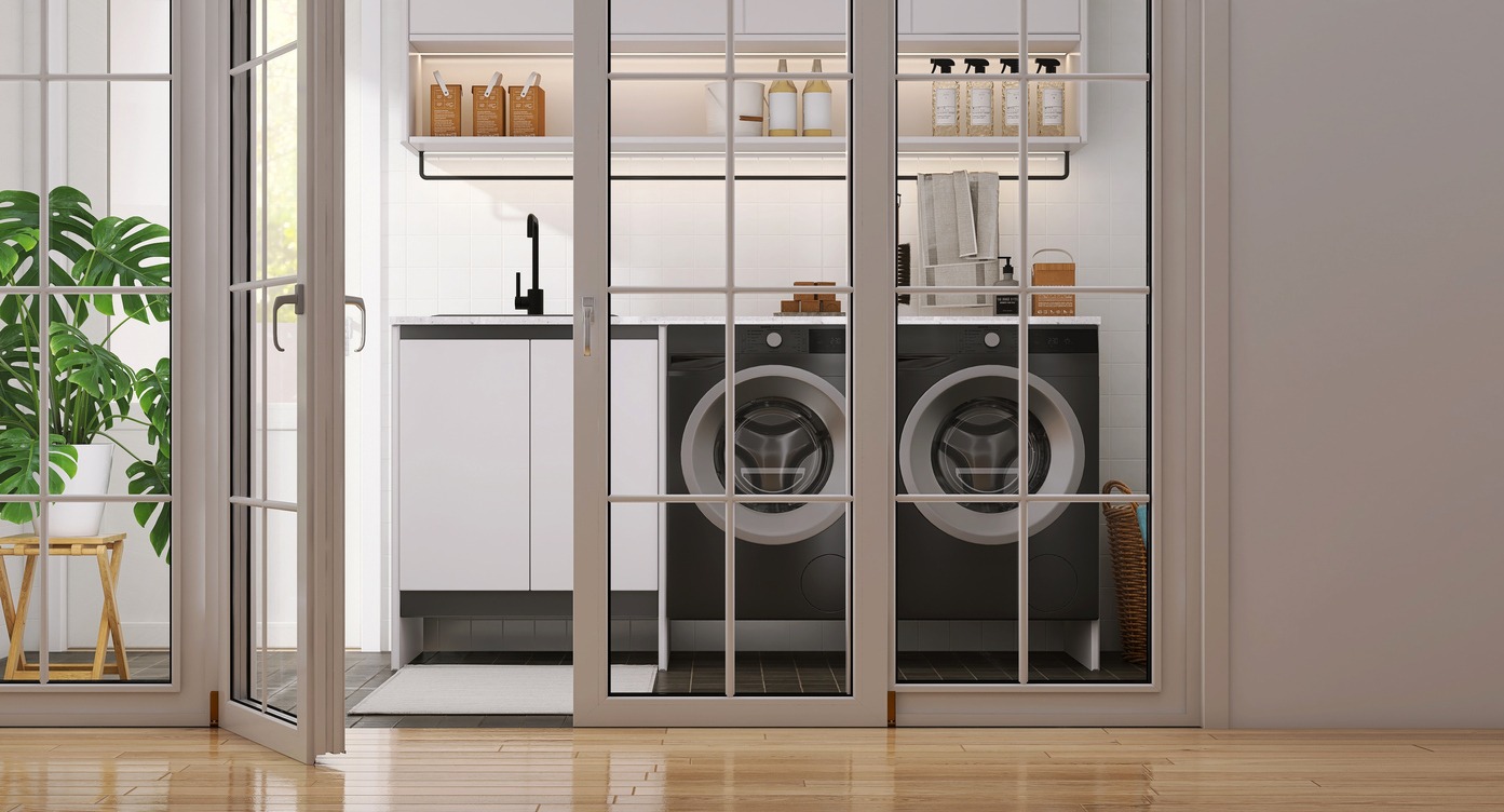 Modern design white frame glass panel lite door of laundry room with two black washing machines, cabinet, cupboard, sink, monstera plant, and tile floor