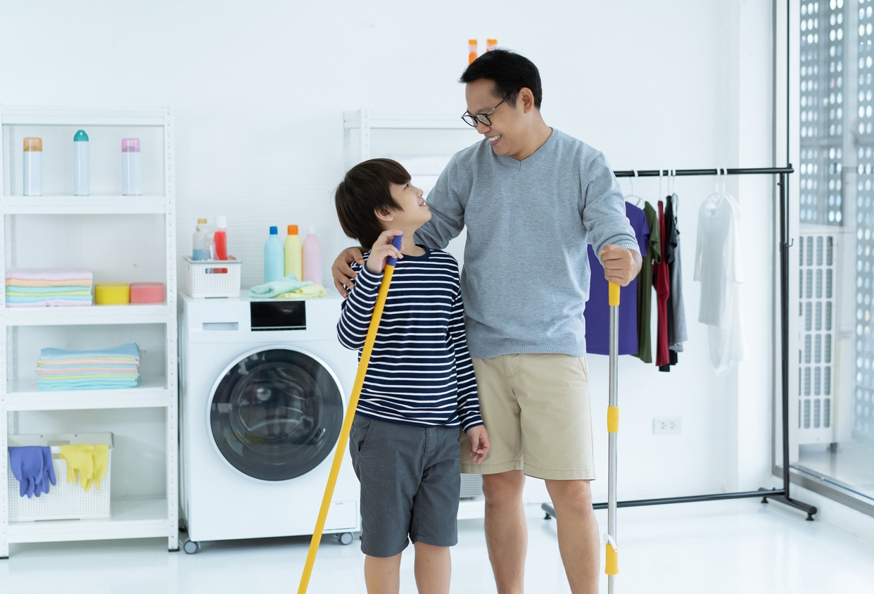 Smiling Asian father and kid little boy son doing household chores cleaning and washing the floor wiping dust with mopping, and looking at each other in the laundry room. Housekeeping and home cleaning concept