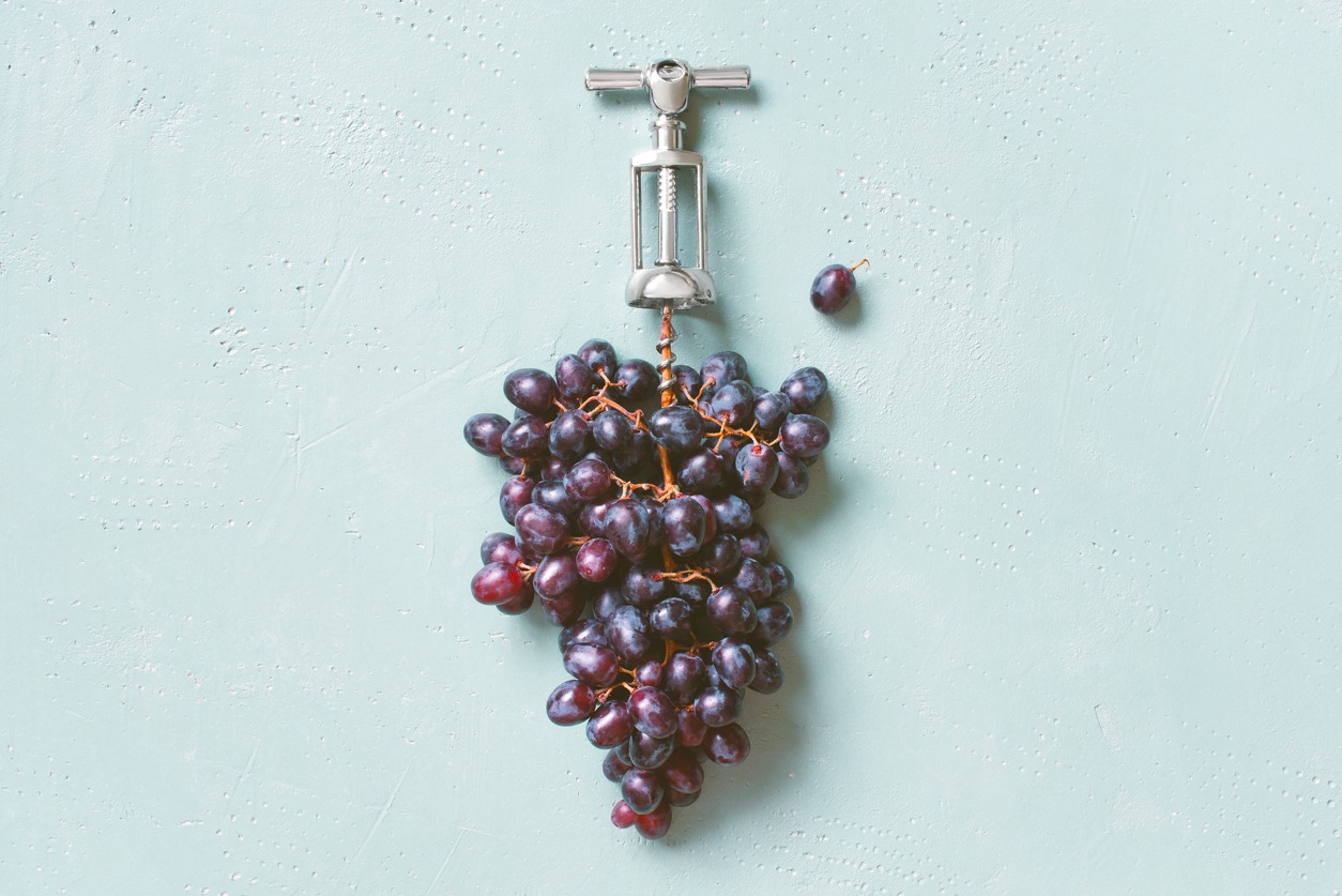 a bunch of grapes with metal corkscrew on a textured blue table