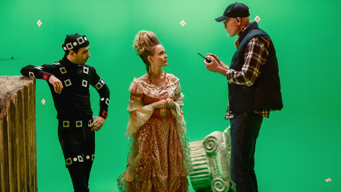 actress wearing renaissance dress and actor wearing motion capture suit listening to movie director explaining the scene