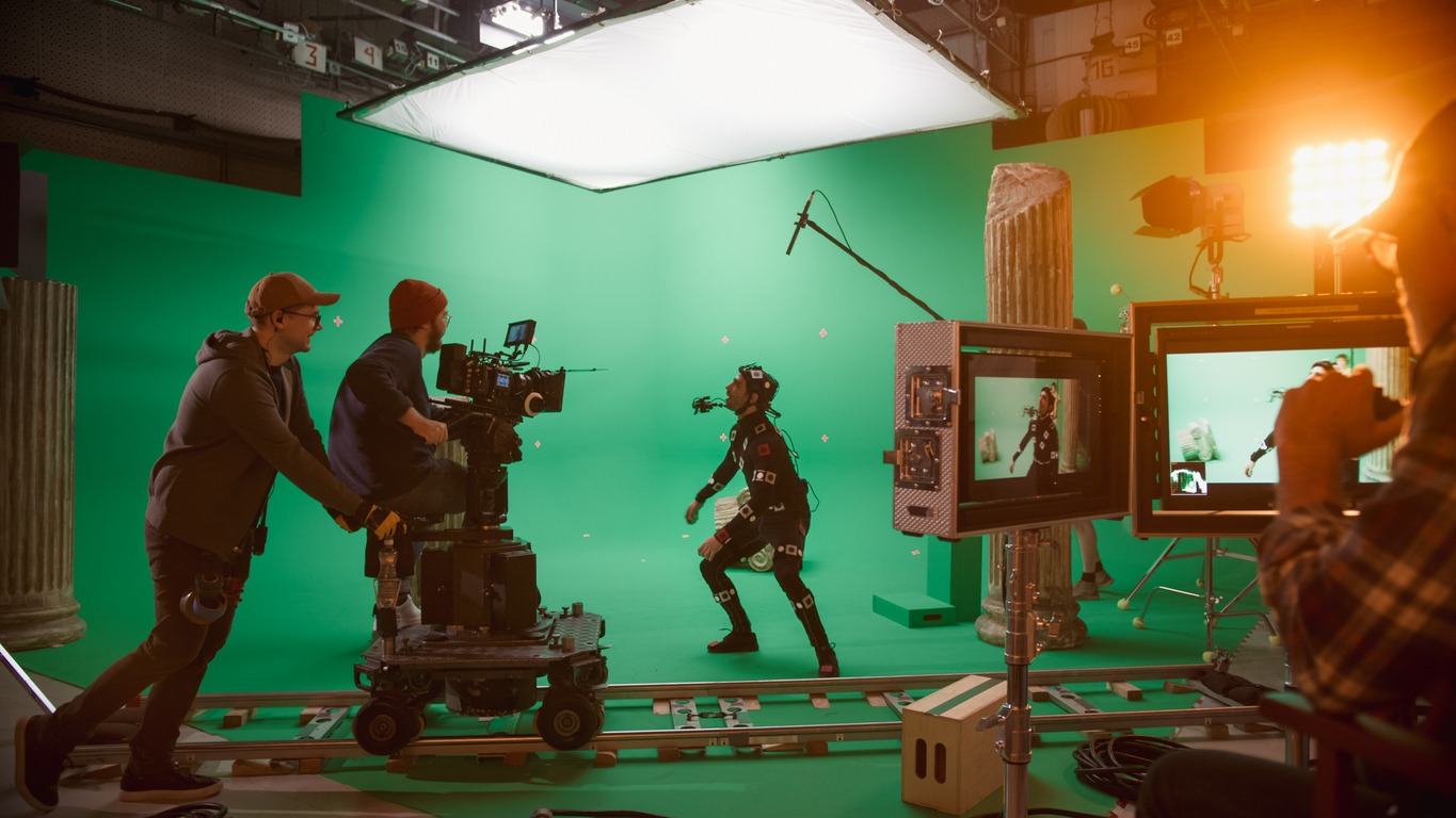 cameraman shooting green screen CGI scene with actor wearing motion tracking suit and head rig