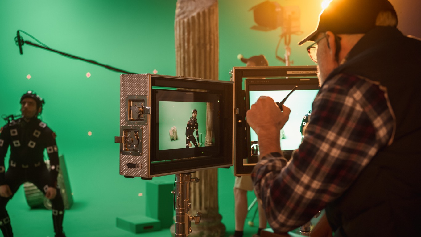 director looking at the actor on the screen wearing a motion tracking suit and head rig