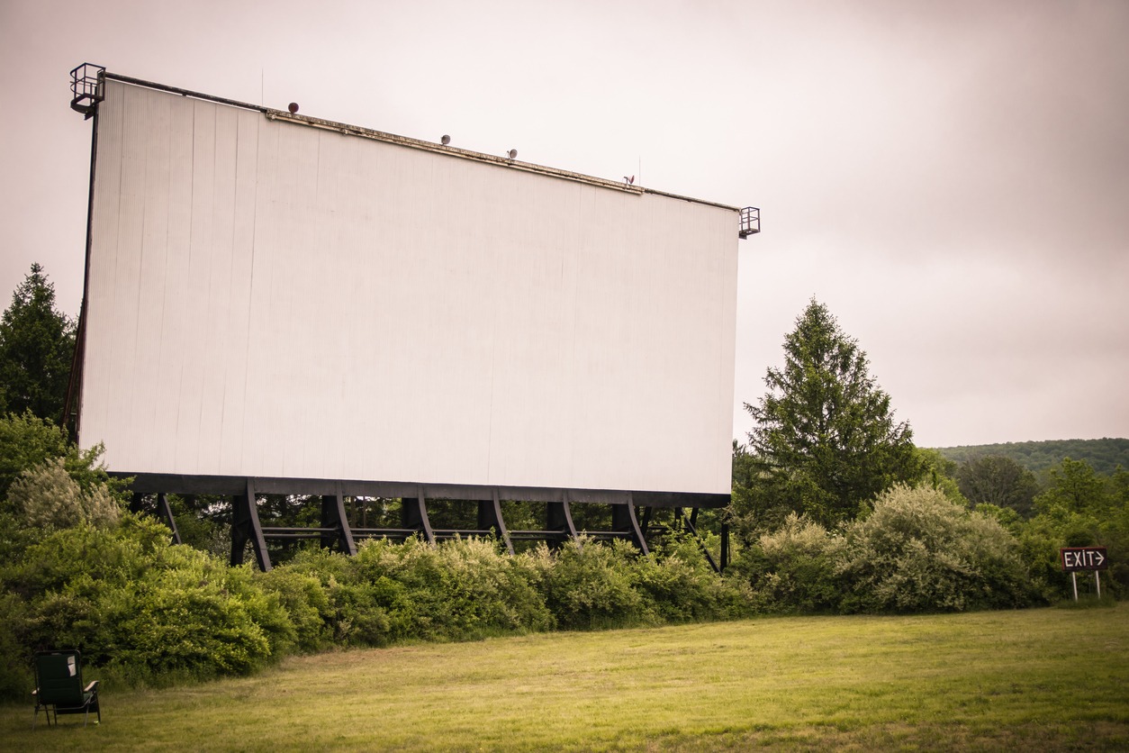 drive-in movie theater screen surrounded by grass and wooded overgrowth