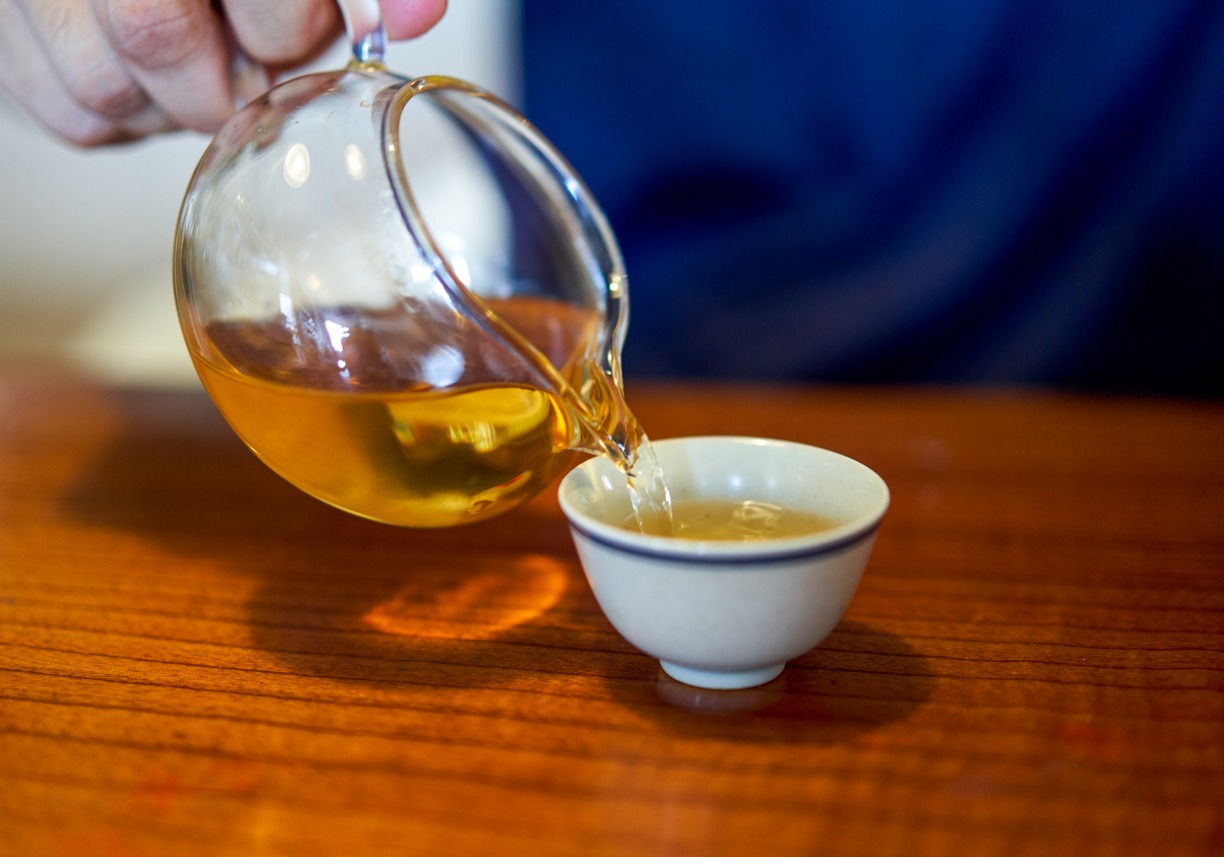 Someone pouring green tea in cups from a glass kettle