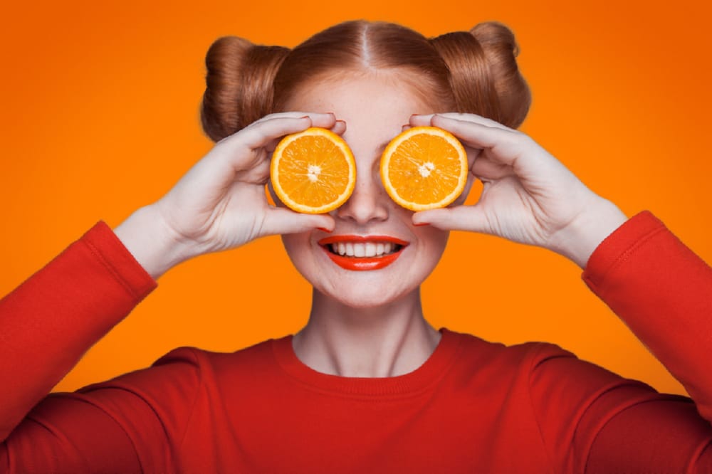 Woman in orange fashion holding two slices of oranges