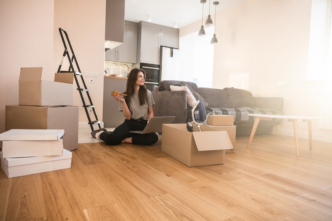 woman sitting on a floor of a new apartment with boxes while eating pizza