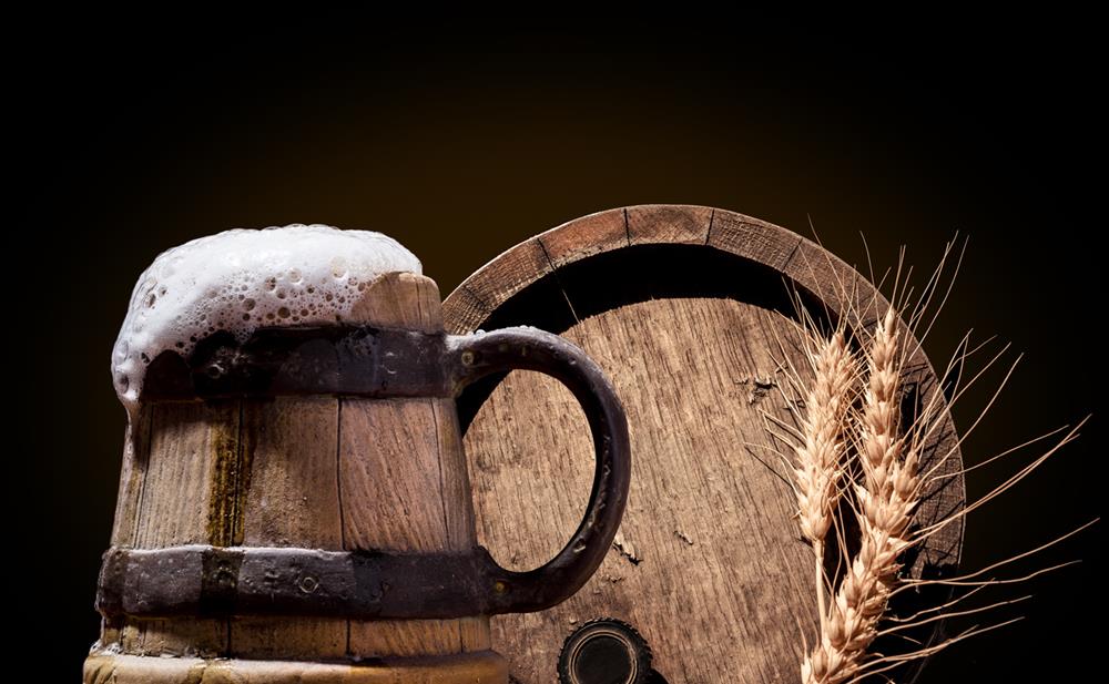 Ancient wooden pint with beer in front of oak barrel with wheat ears