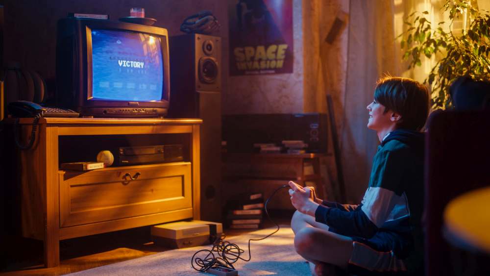 Boy playing 80s 8-bit arcade space shooter video game on a console at home