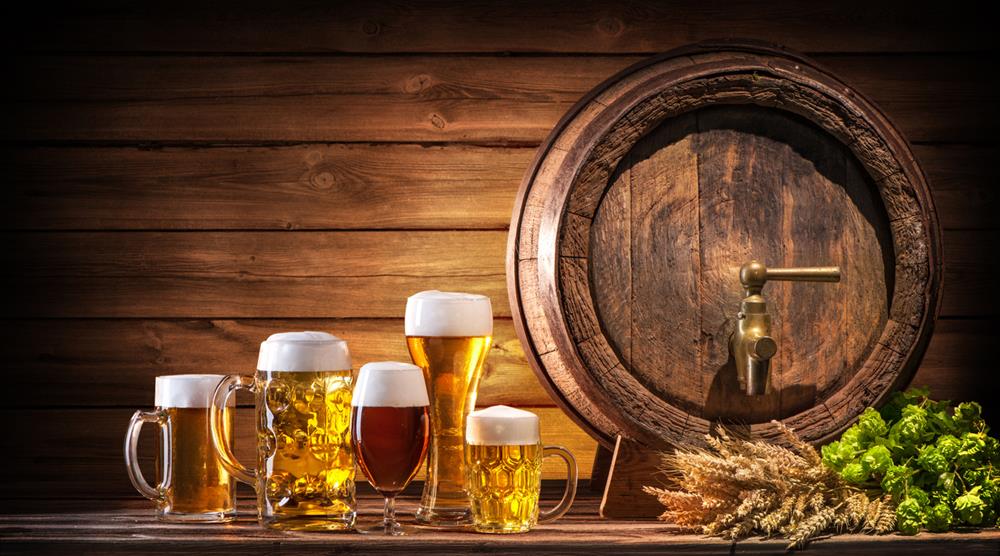 Glasses of beer by the wooden barrel and beer ingredients