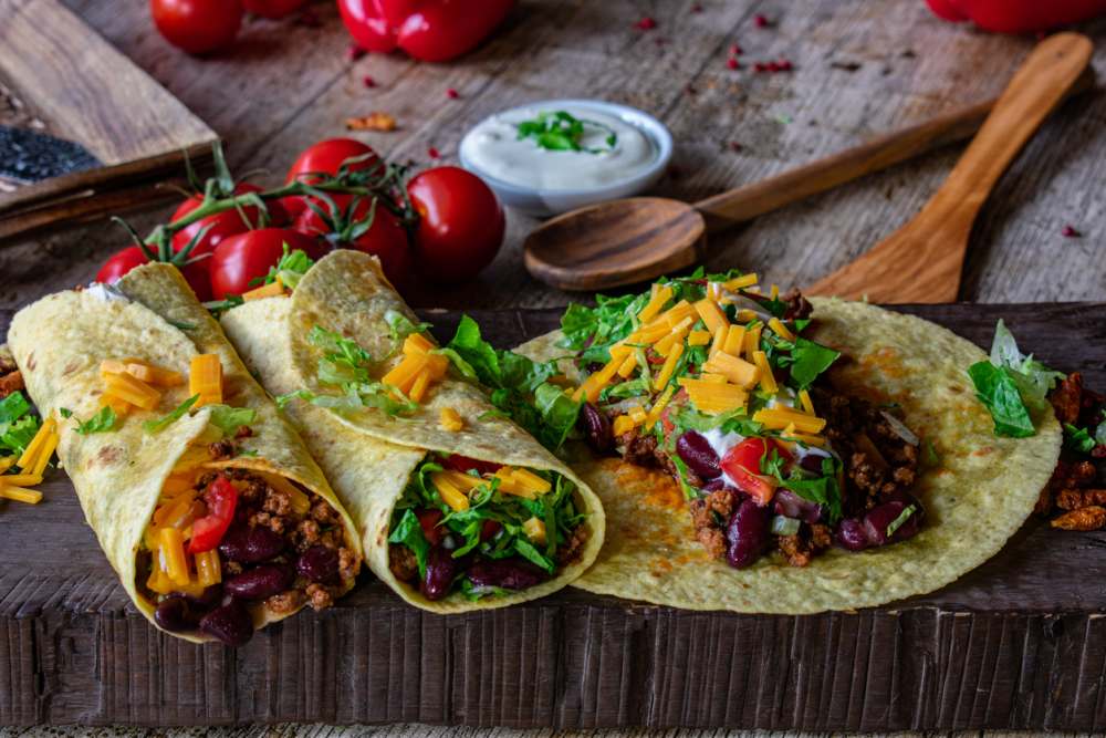 Homemade burritos with minced meat and beans filling served on a wooden rustic board