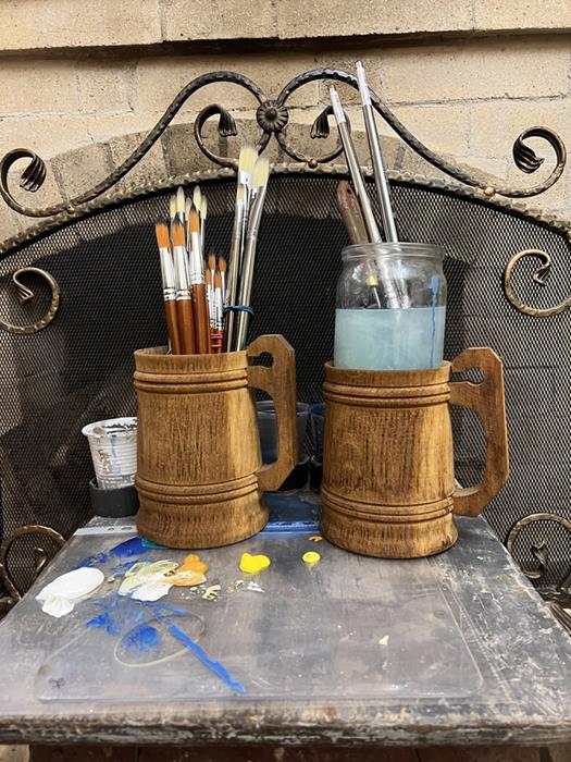 Two large wooden mugs beer pints with tassels handles holding paint brushes