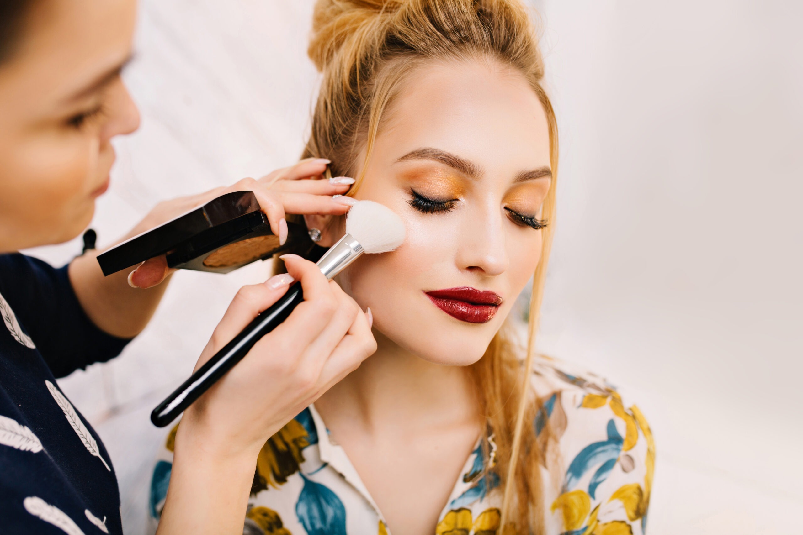Closeup portrait charming blonde woman preparing to celebration party in beauty salon Making makeup professional stylist red lips luxury look satisfaction fashionable model